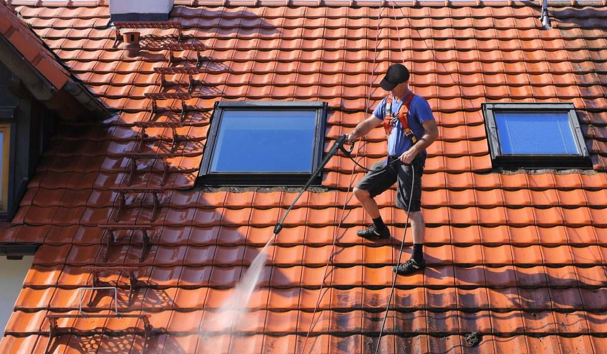 Ouvrier nettoyant au jet une toiture en tuiles orange équipée de fenêtres de toit