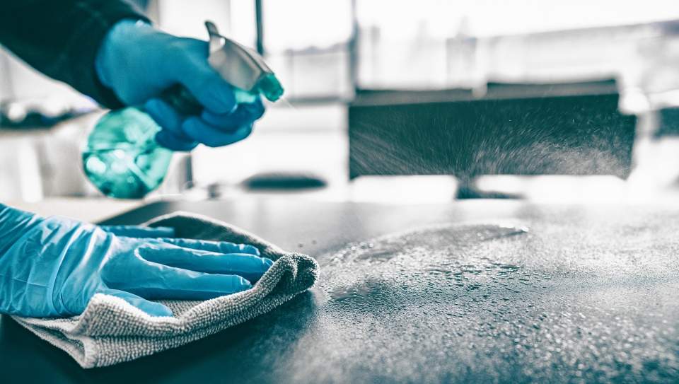 Mains gantées pulvérisant un produit désinfectant sur une surface