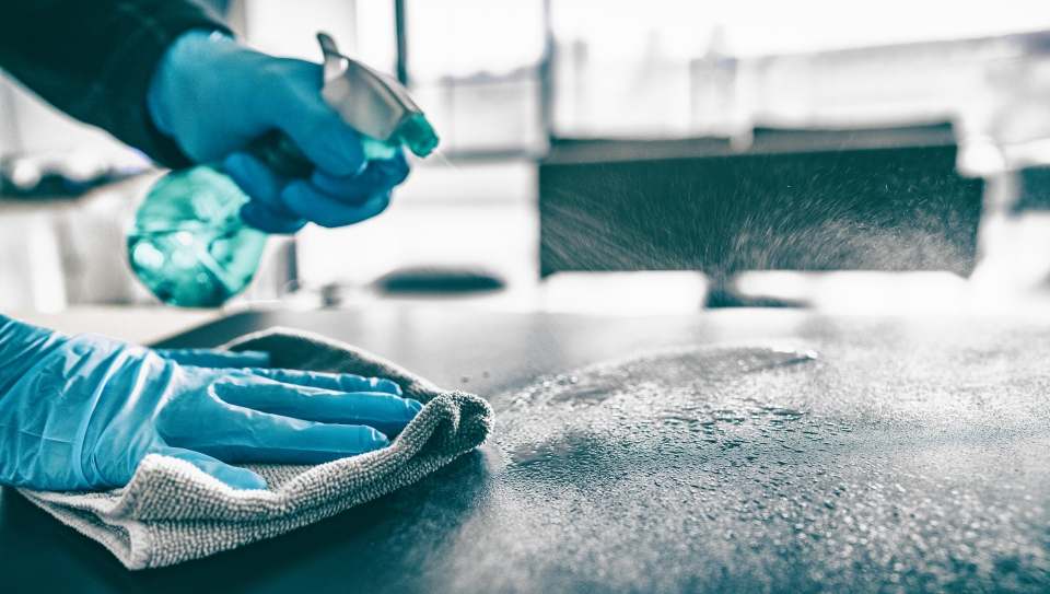 Mains gantées désinfectant une surface avec un pulvérisateur