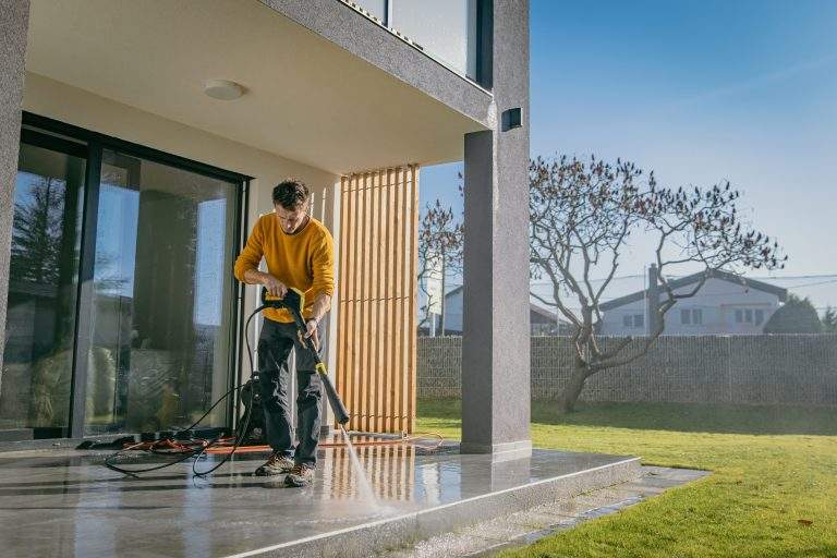 Homme nettoyant une terrasse carrelée devant une maison moderne